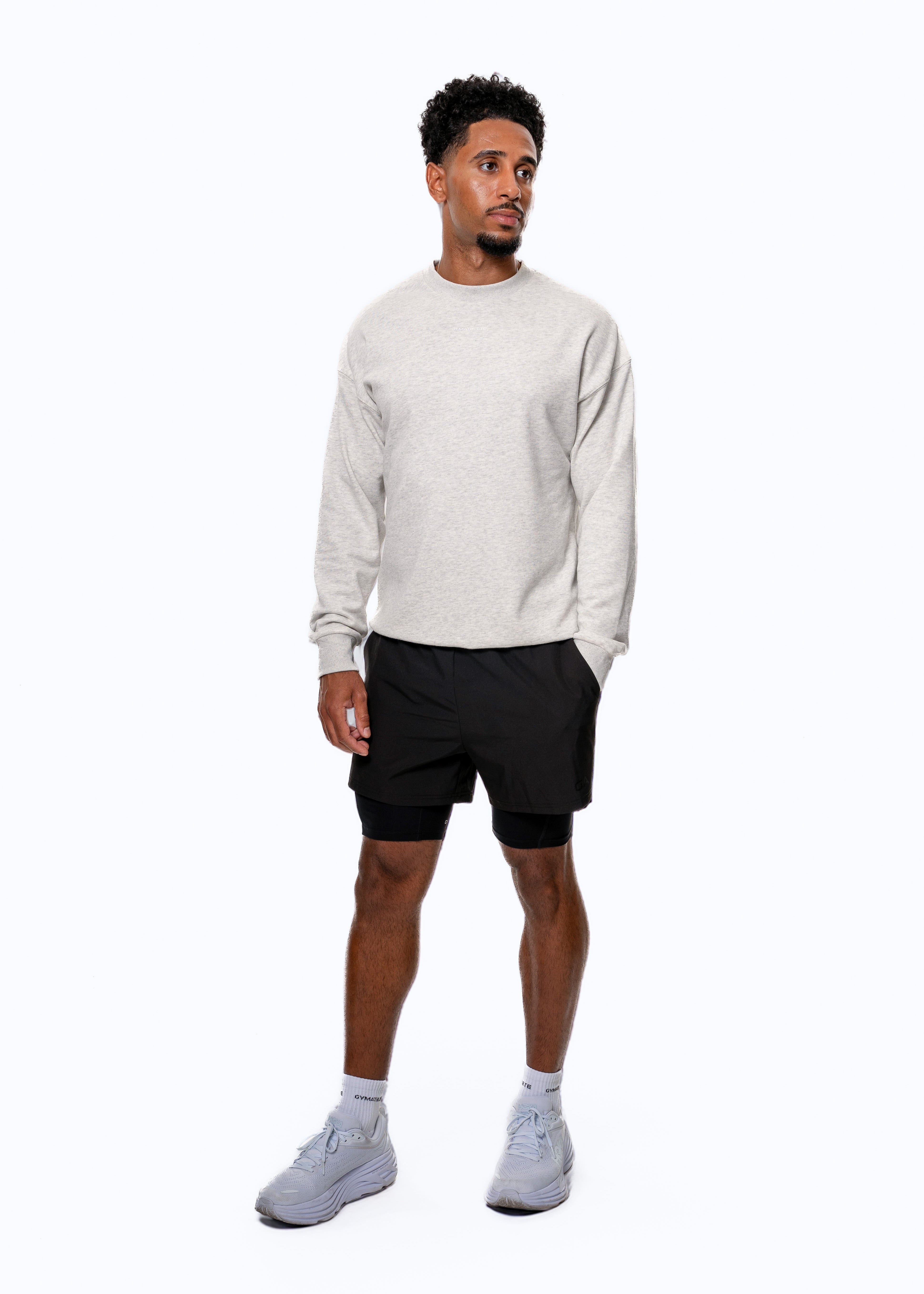 Man wearing a light gray sweater, black shorts, and white sneakers on a white background. Gymathlete-Elevate Sweatshirt
