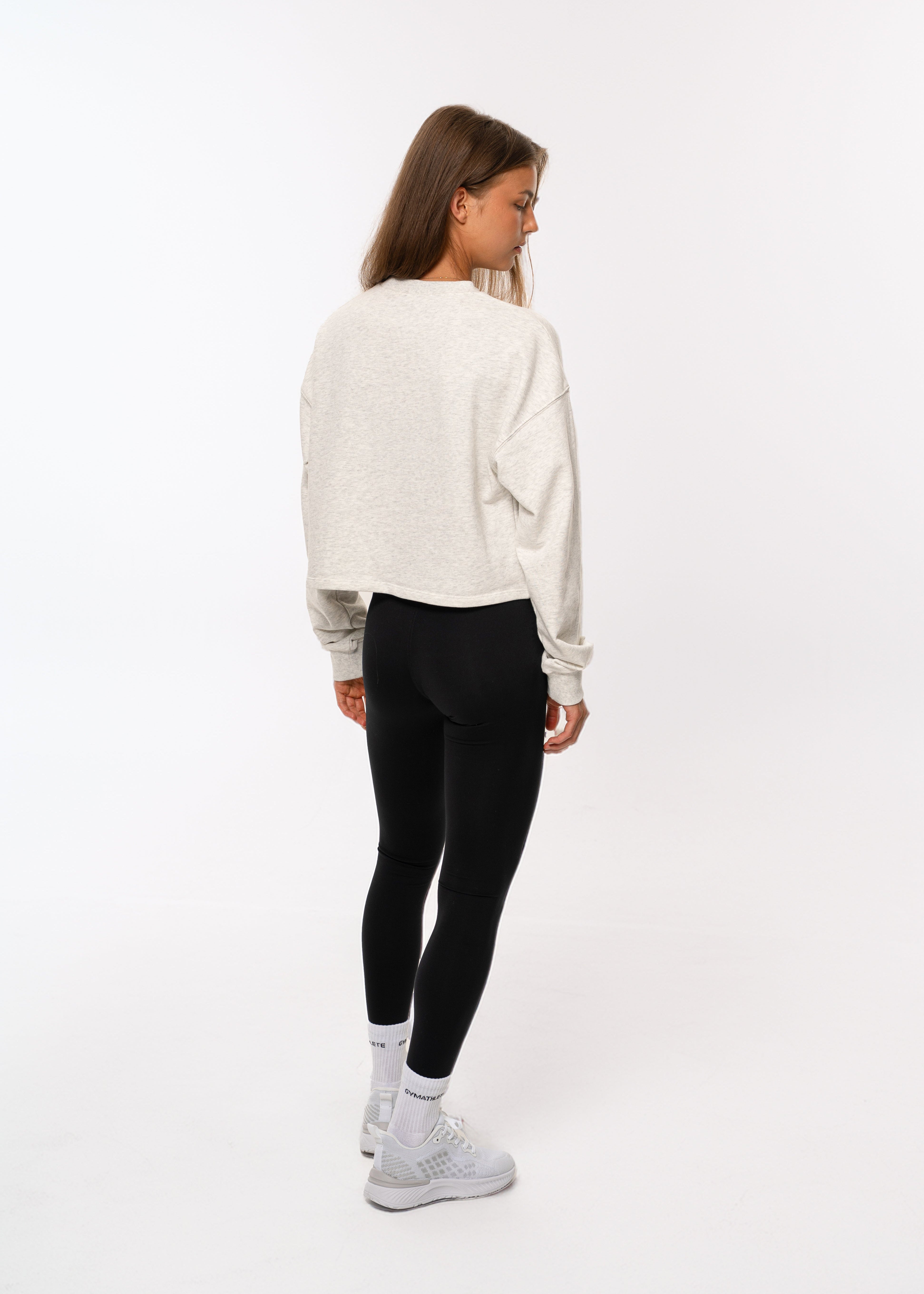 Person wearing a white sweater and black leggings on a white background. Women - Gymathlete - Flow Crop Sweatshirt - White melange