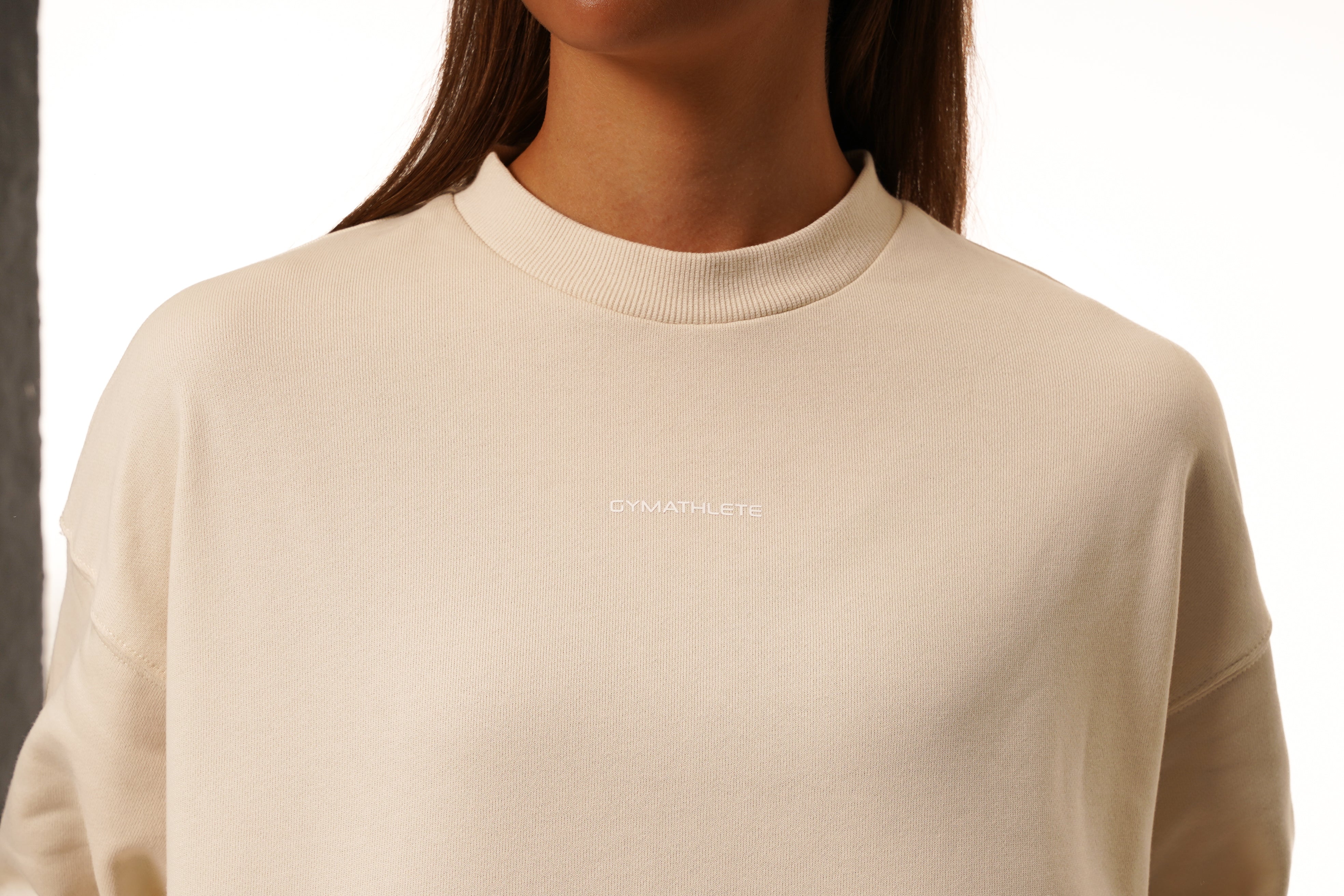 Beige sweater with a brand logo worn by a person on a white background. Women - Gymathlete - Flow Crop Sweatshirt - Beige