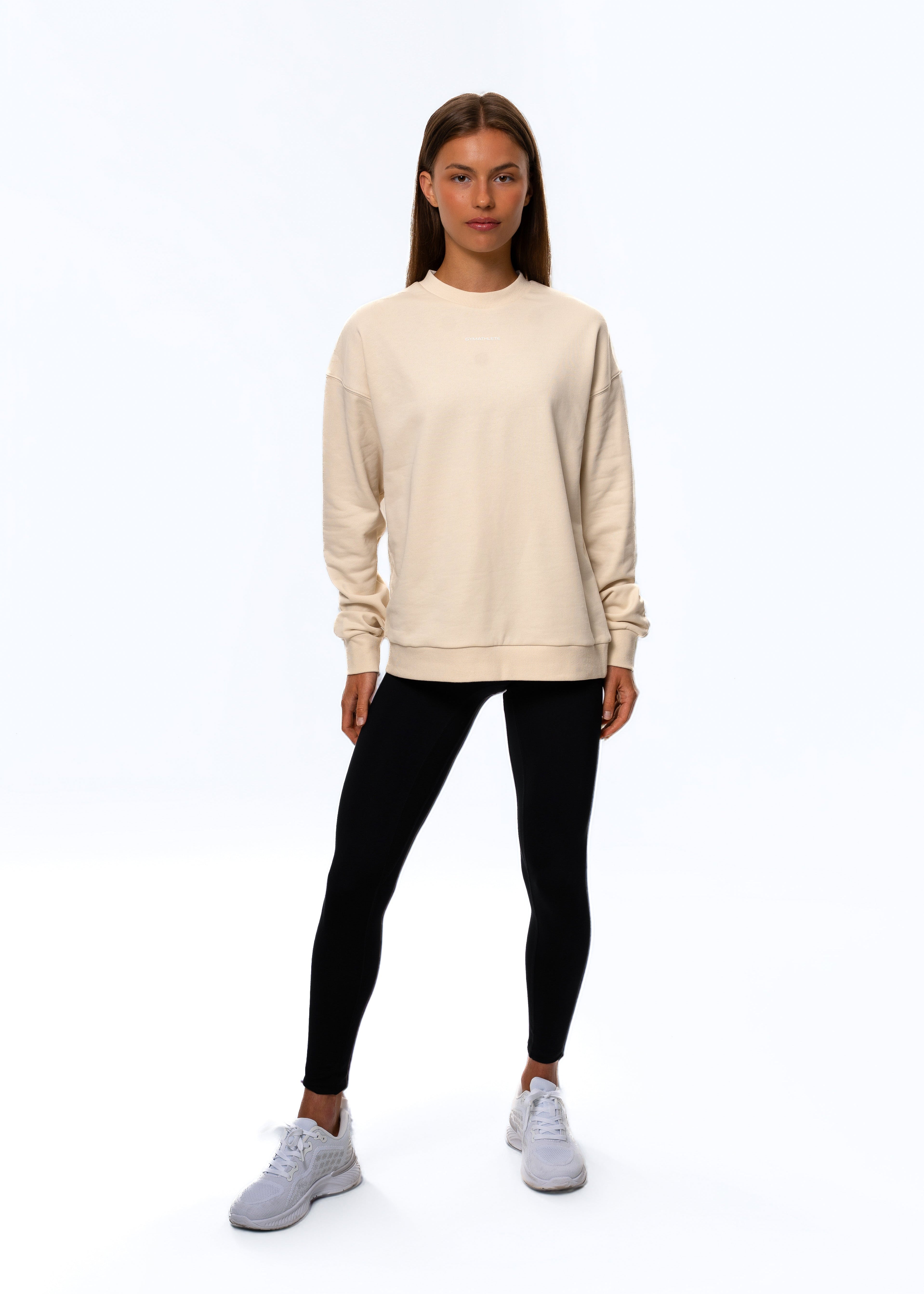 Person wearing a beige sweatshirt, black leggings, and white sneakers on a white background. Women - Gymathlete - Flow Sweatshirt - Beige.
