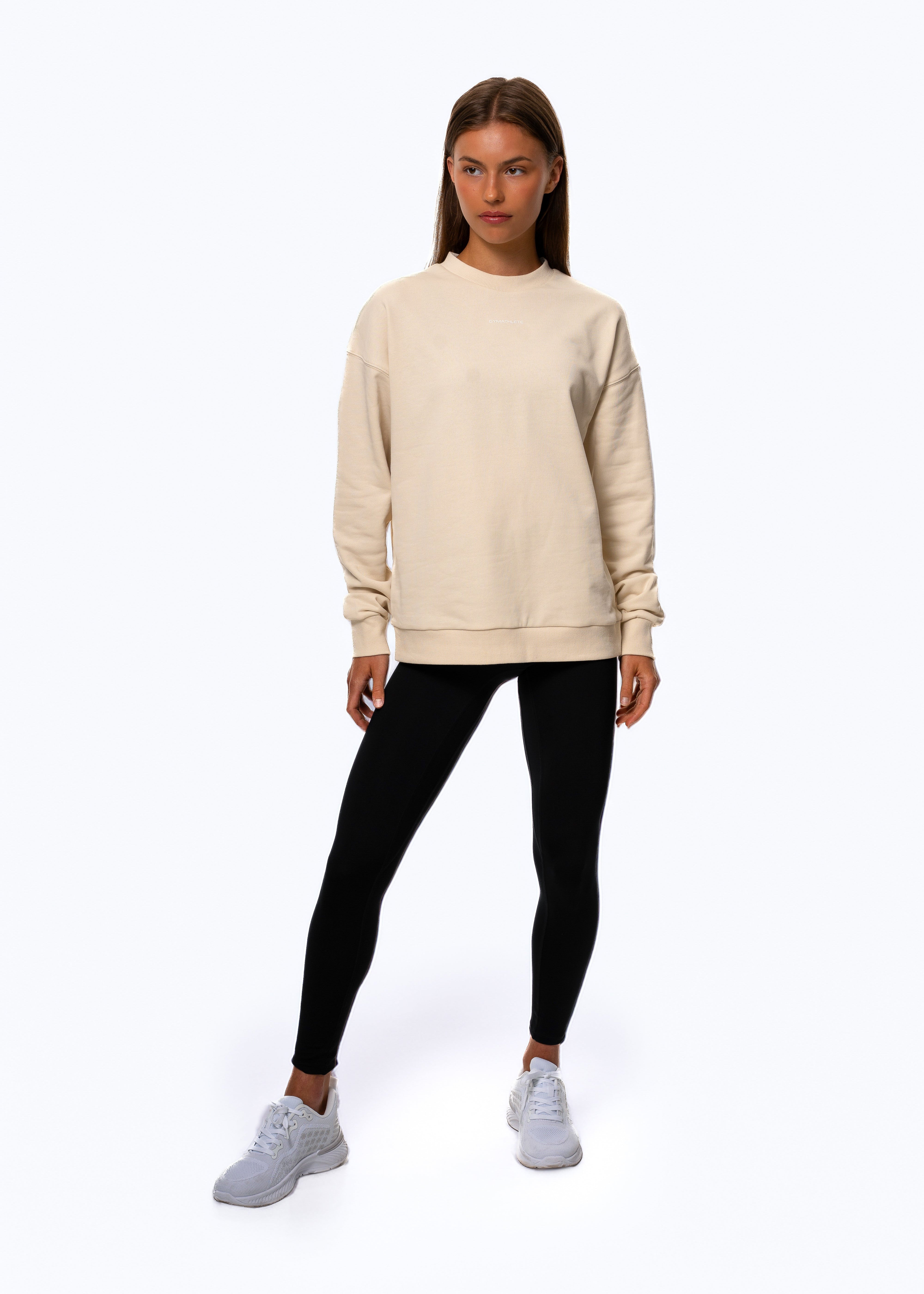 Woman wearing a beige sweatshirt and black leggings on a white background. Women - Gymathlete - Flow Sweatshirt - Beige.