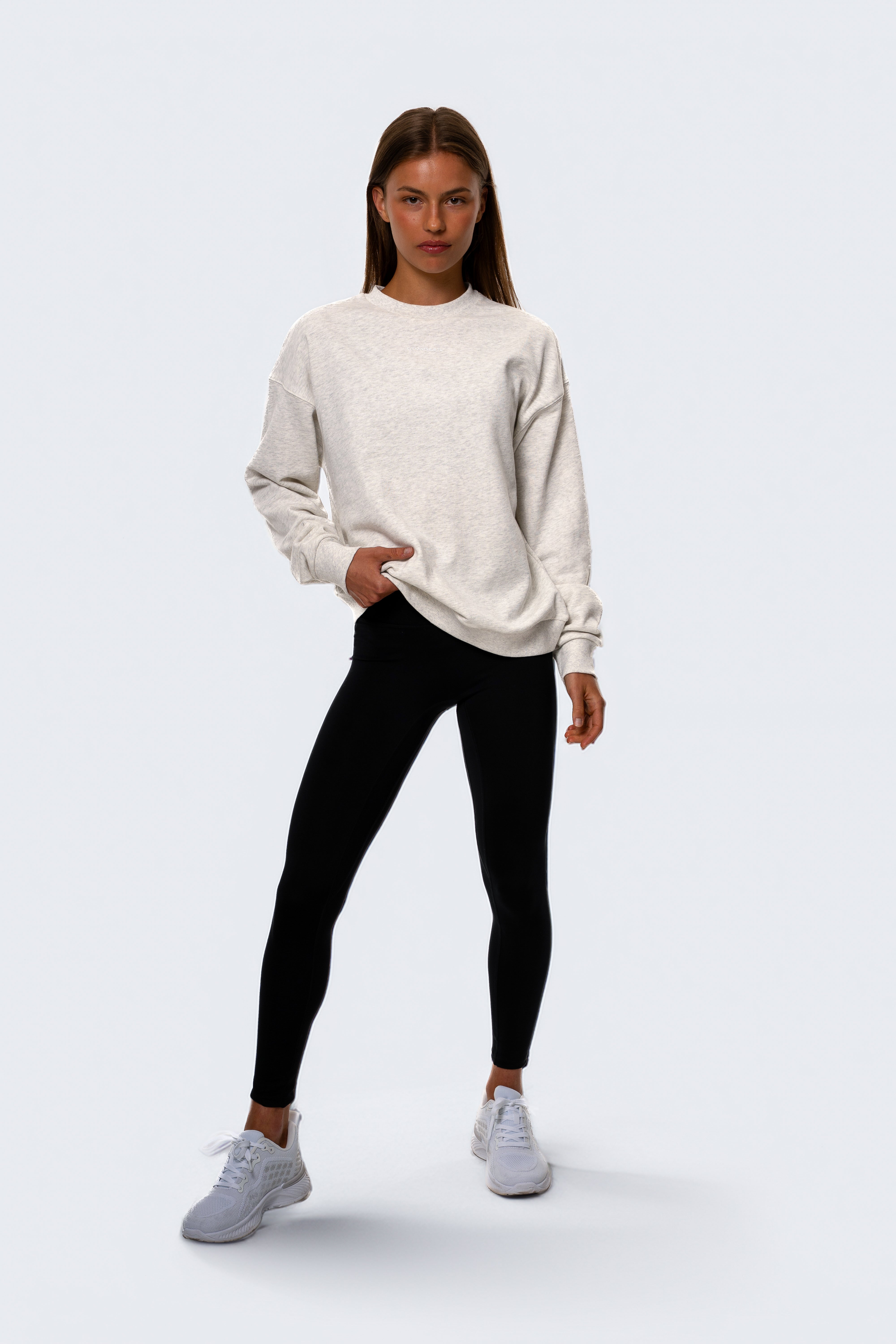 Woman wearing a white sweatshirt, black leggings, and gray sneakers on a white background. Women - Gymathlete - Flow Sweatshirt - White melange.