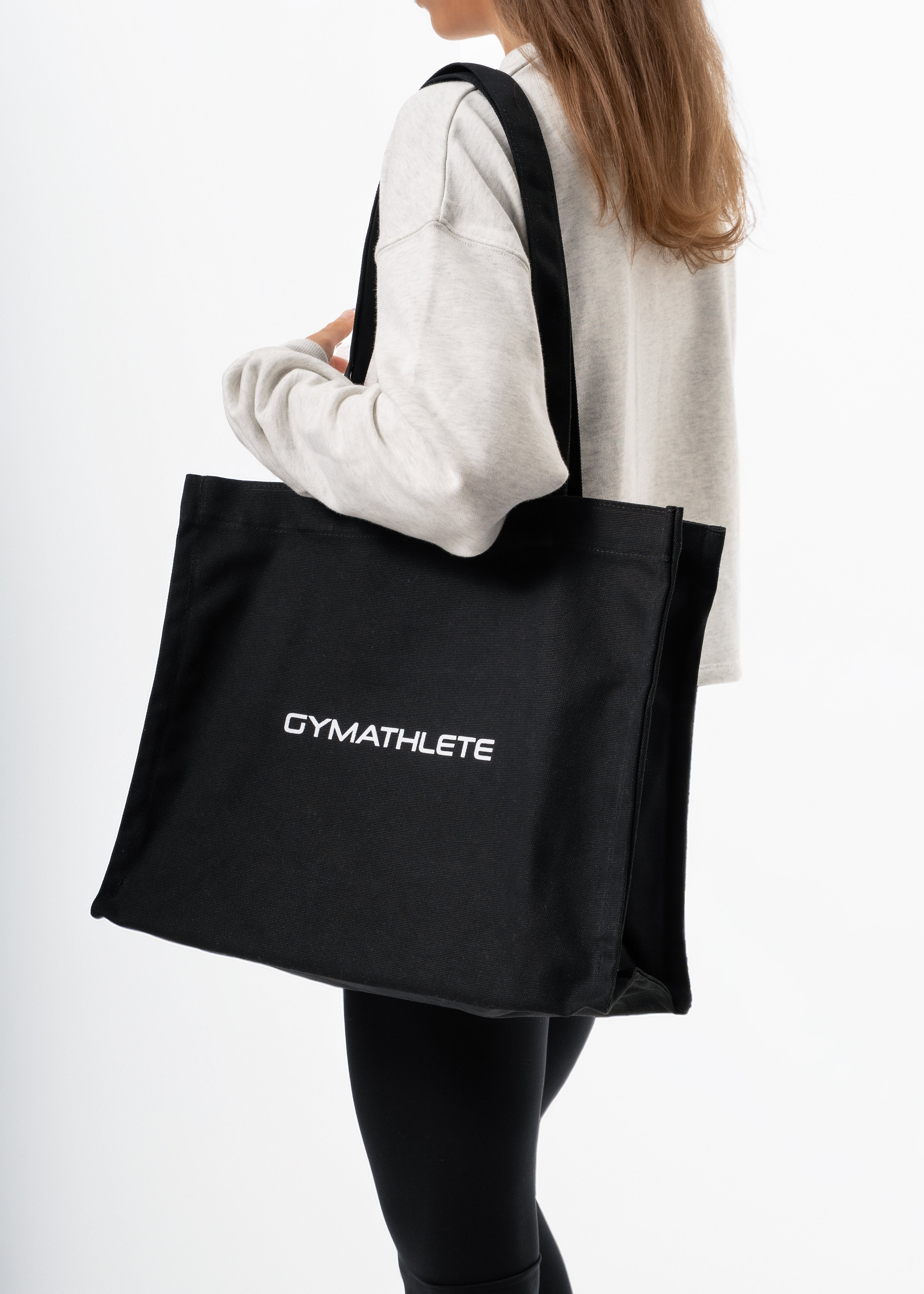Person holding a black tote bag with 'GYMATHLETE' branding on a white background.
Gymathlete Balance tote