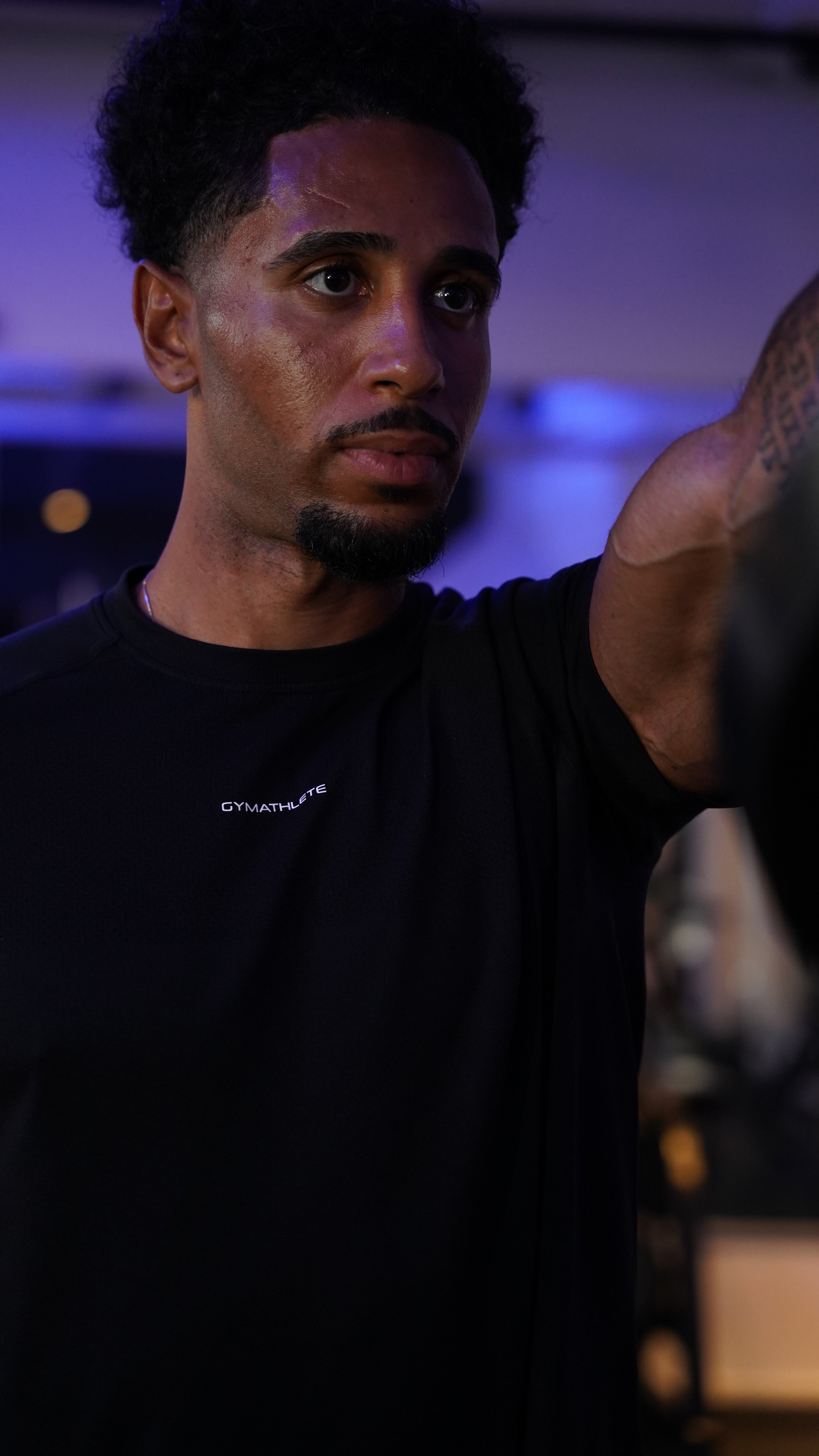 Man wearing a black t-shirt with a brand logo, standing against a blurred background.- Gymathlete, Elevate T-shirt, man, men, workout, gym, athleisure
