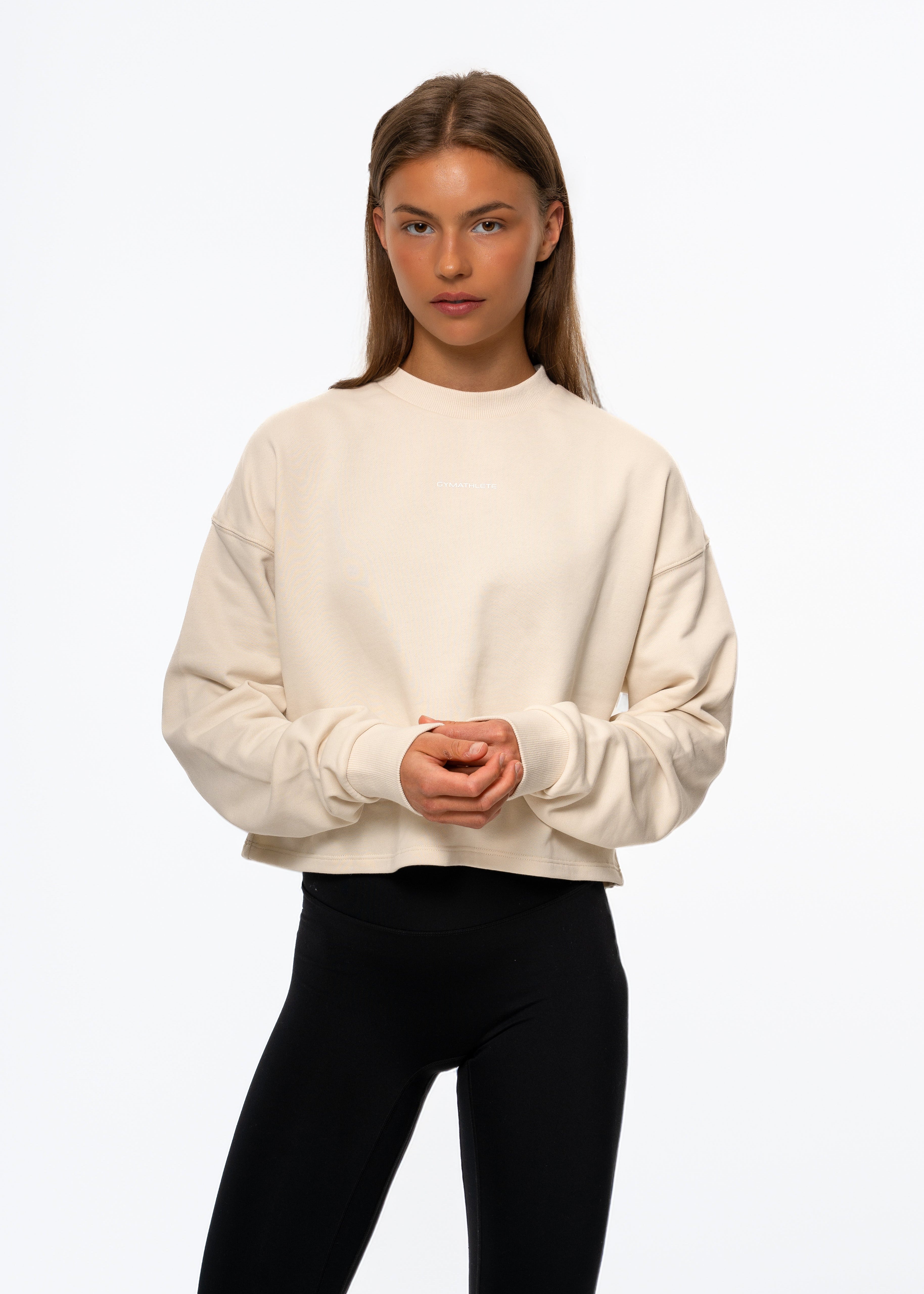 Woman wearing a beige sweater and black pants on a white background. Gymathlete Flow Crop Sweatshirt. Women. Activewear.