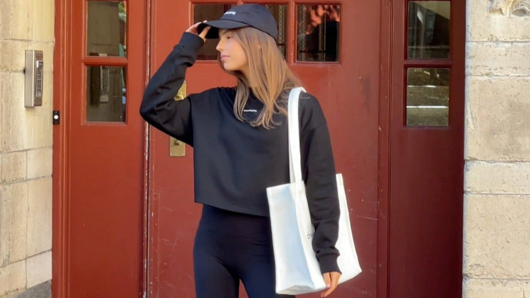 Woman in black outfit with white bag standing in front of a red door. Gymathlete - Balance Tote bag - women.