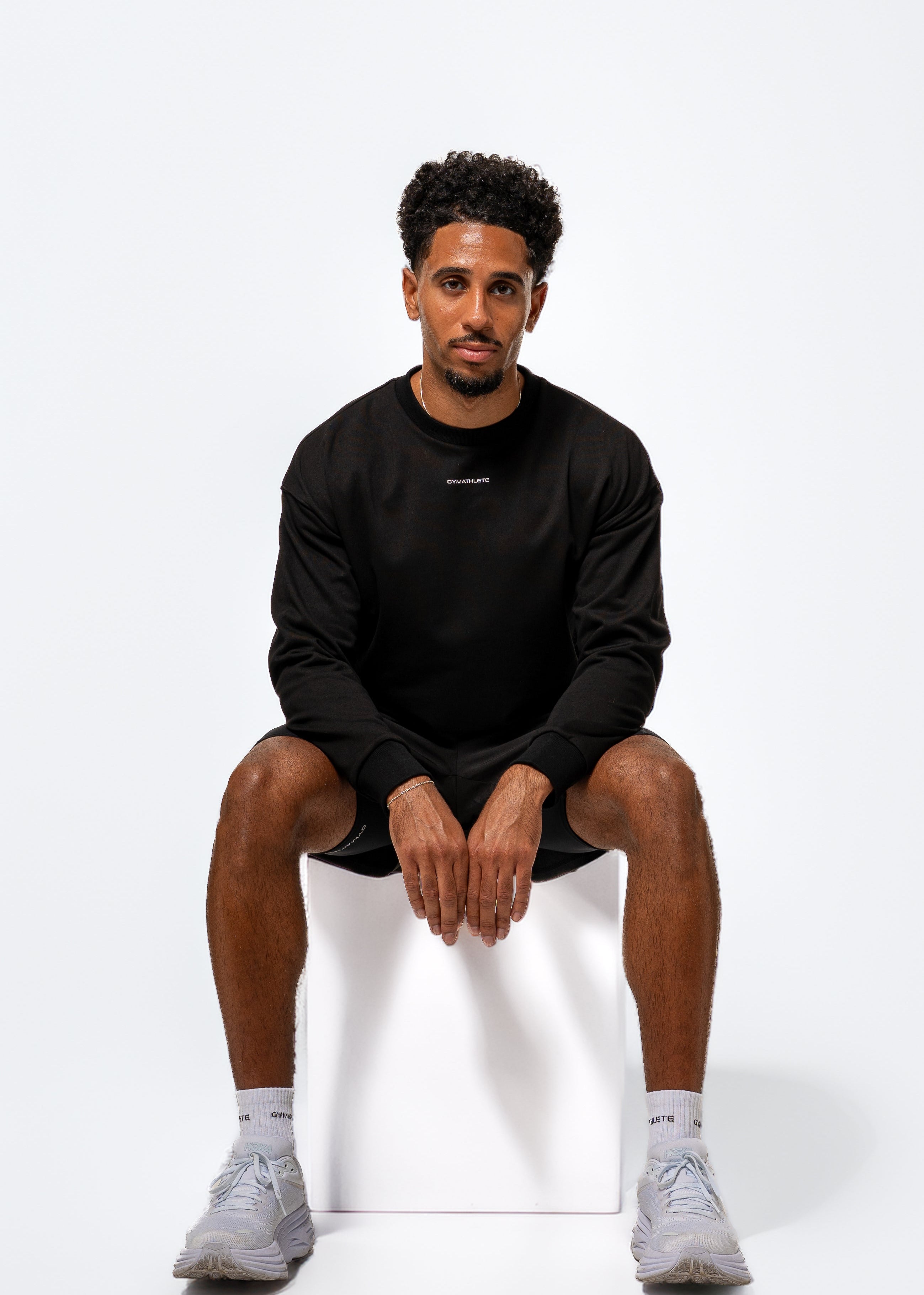 Man wearing a black sweatshirt and shorts with white socks on a white background. Gymathlete, Eelevate Sweatshirt