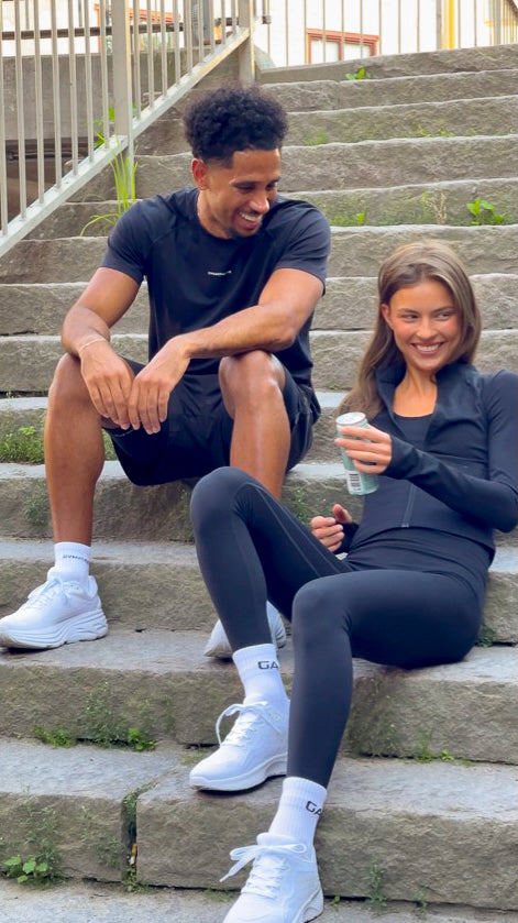 Two people sitting on stone steps outdoors, wearing matching outfits. - Gymathlete - women - men - Endurance socks - Elevate Sweatshirt - happy - laughing.