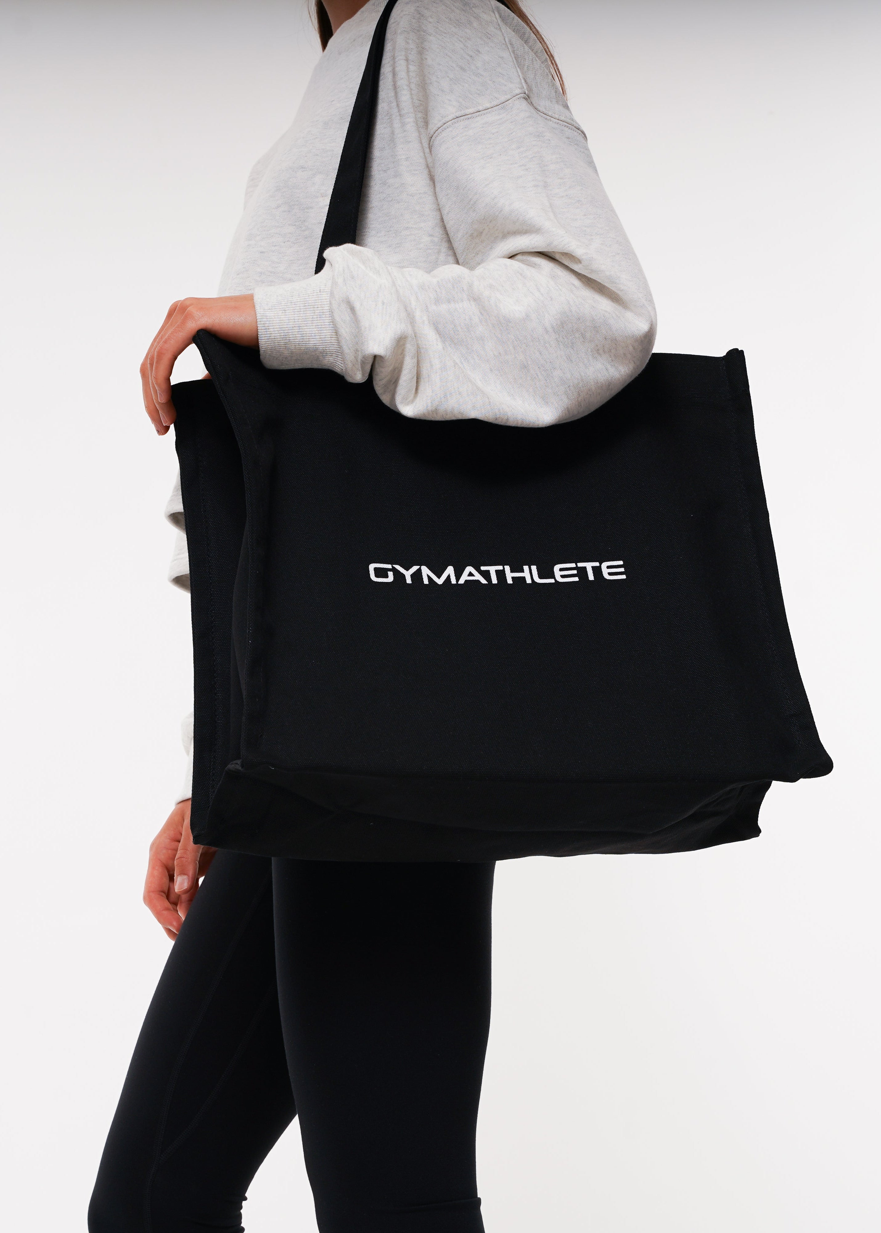 Person holding a black tote bag with 'GYMATHLETE' branding on a white background. 

Women - Black - Gymathlete Balance Tote bag