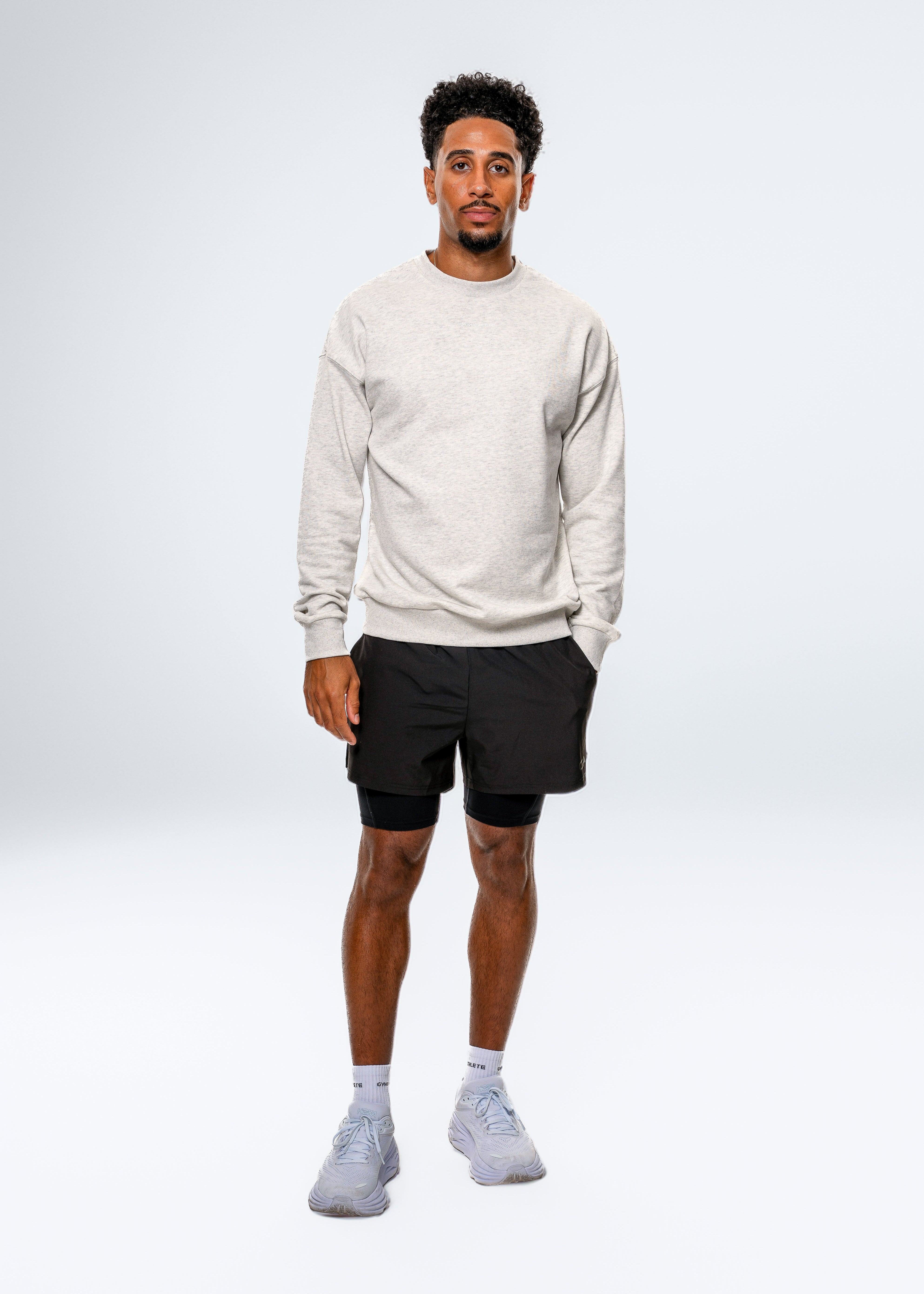 Man wearing a light gray sweatshirt, black shorts, and white sneakers on a white background. Gymathlete - Elevate Sweatshirt - men