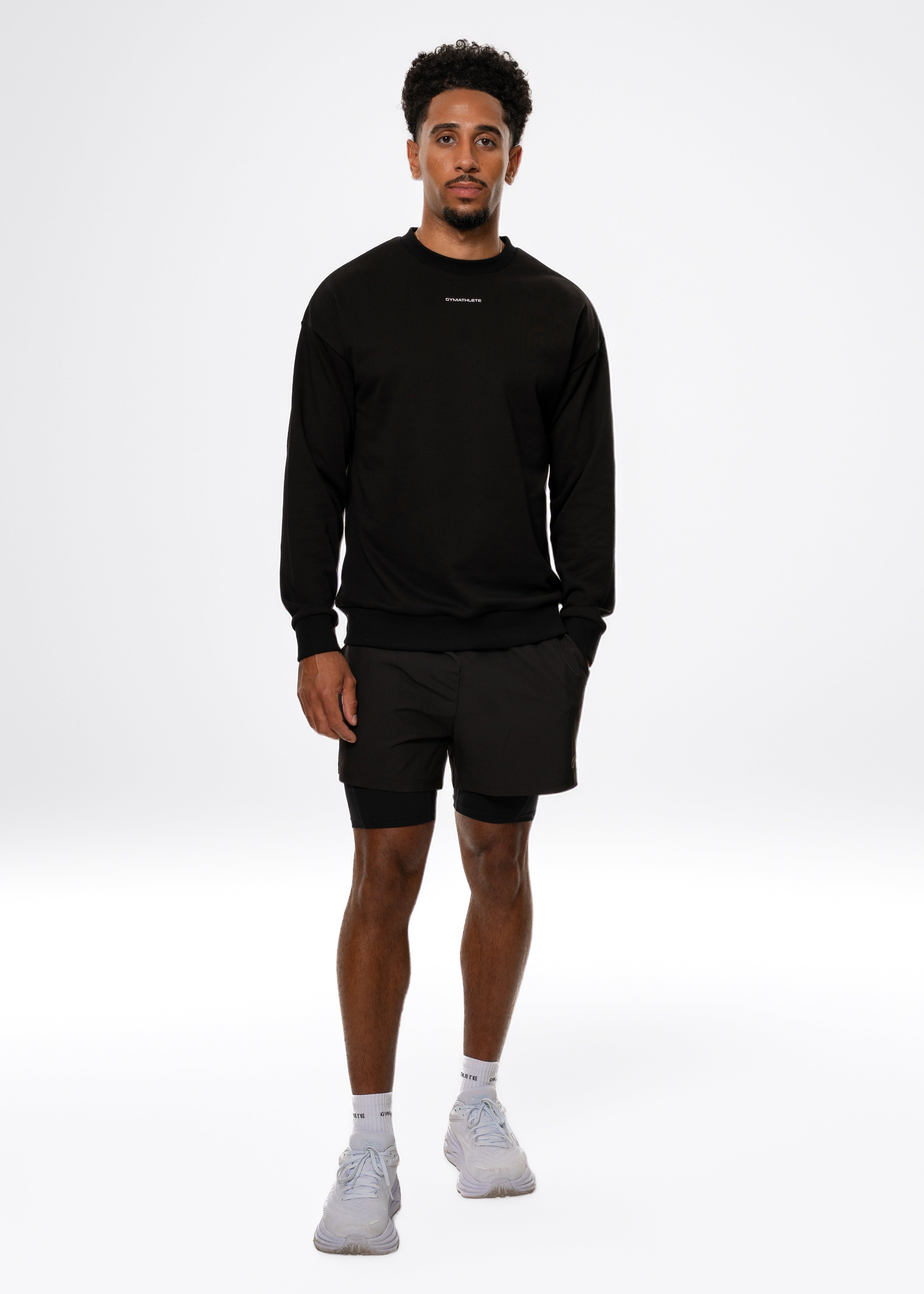 Man wearing a black sweatshirt and shorts with white socks on a white background. Gymathlete, Eelevate Sweatshirt