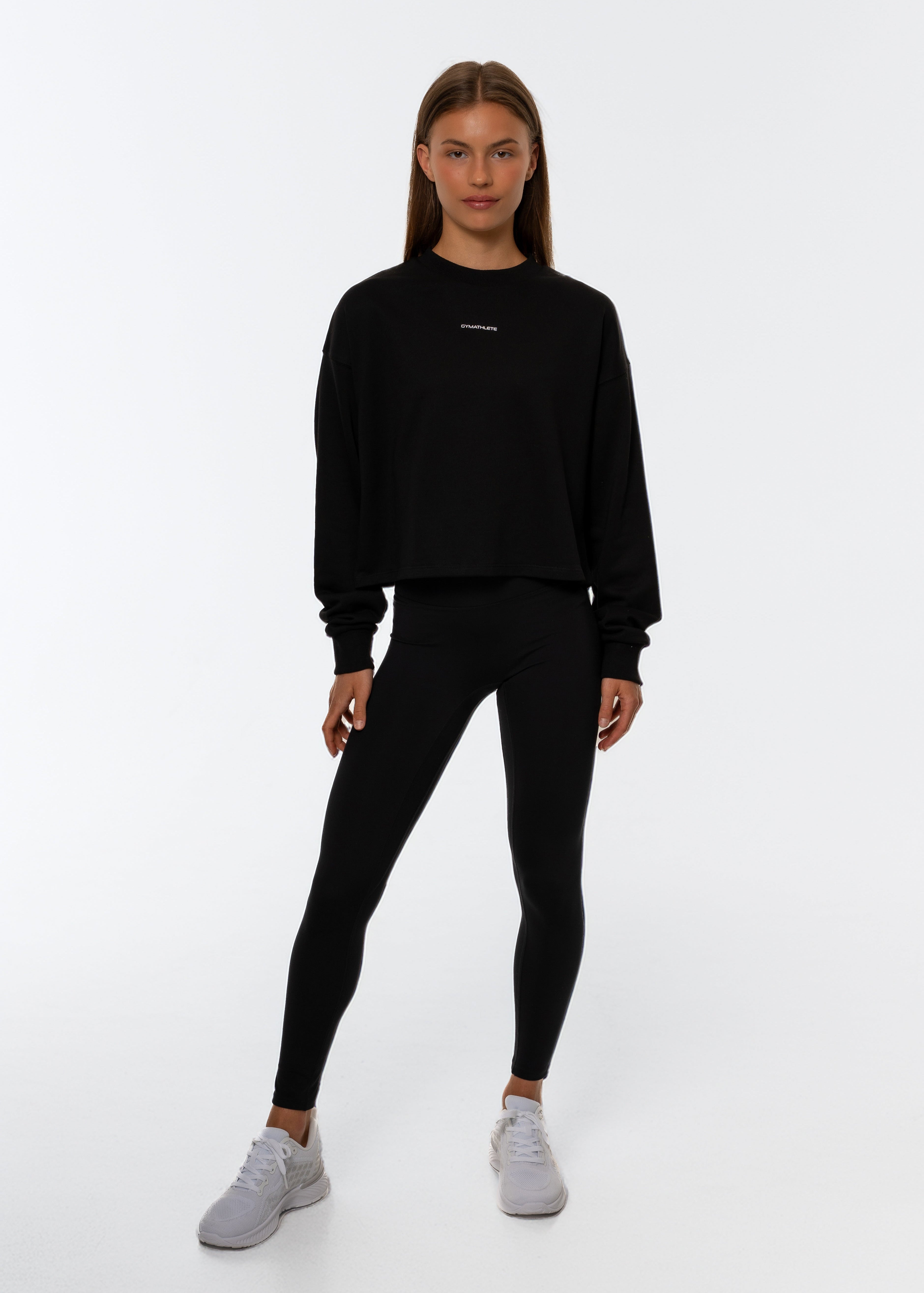 Person wearing a black sweatshirt with a white background and leggings. Gymathlete Flow crop sweatshirt