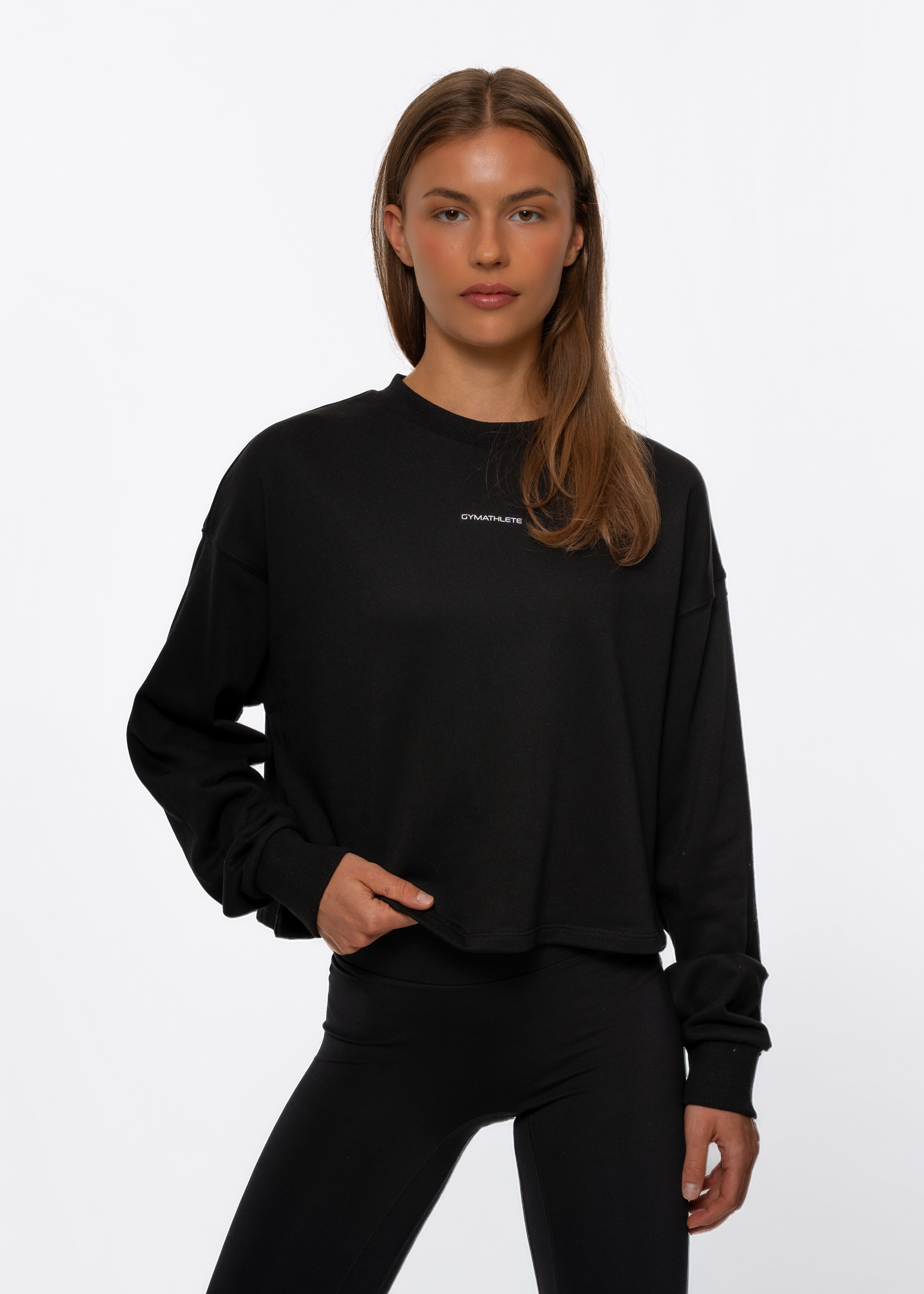 Woman wearing a black long-sleeve top on a white background. Gymathlete, Flow crop sweatshirt.