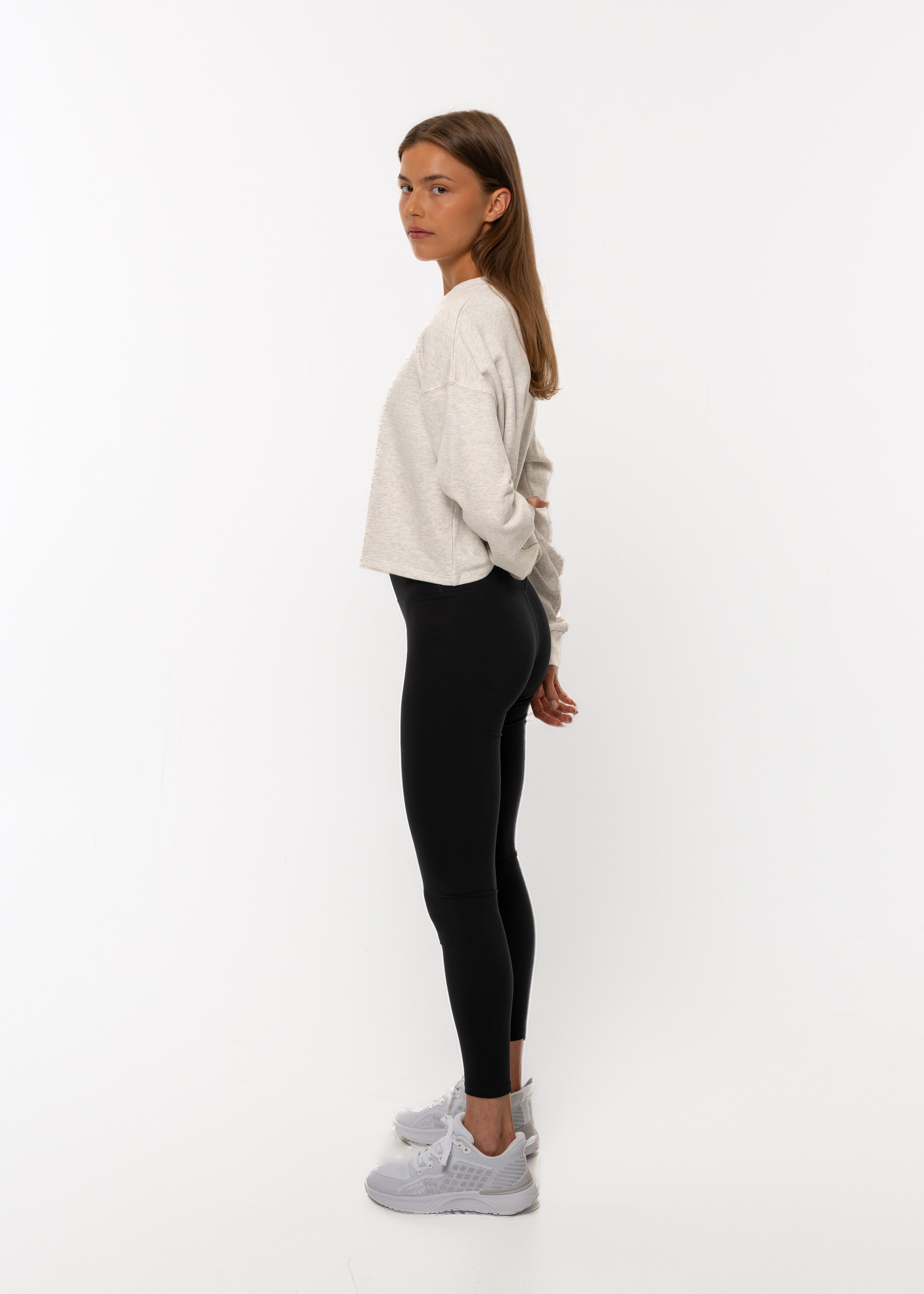 Woman wearing a light-colored sweater and black leggings on a white background. Gymathlete, Flow crop sweatshirt