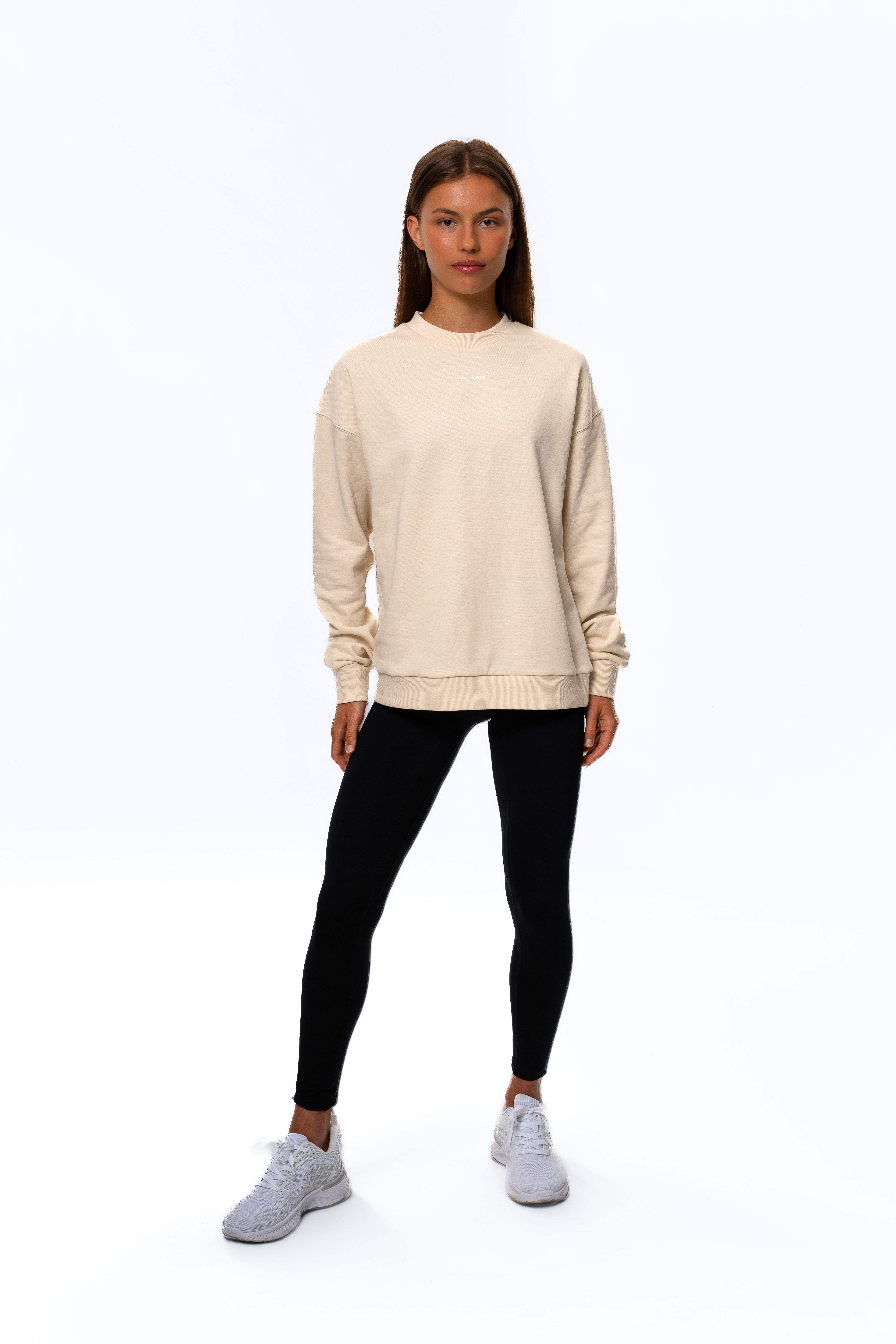 Person wearing a beige sweatshirt, black leggings, and white sneakers on a white background. Women - Gymathlete - Flow Sweatshirt - Beige.