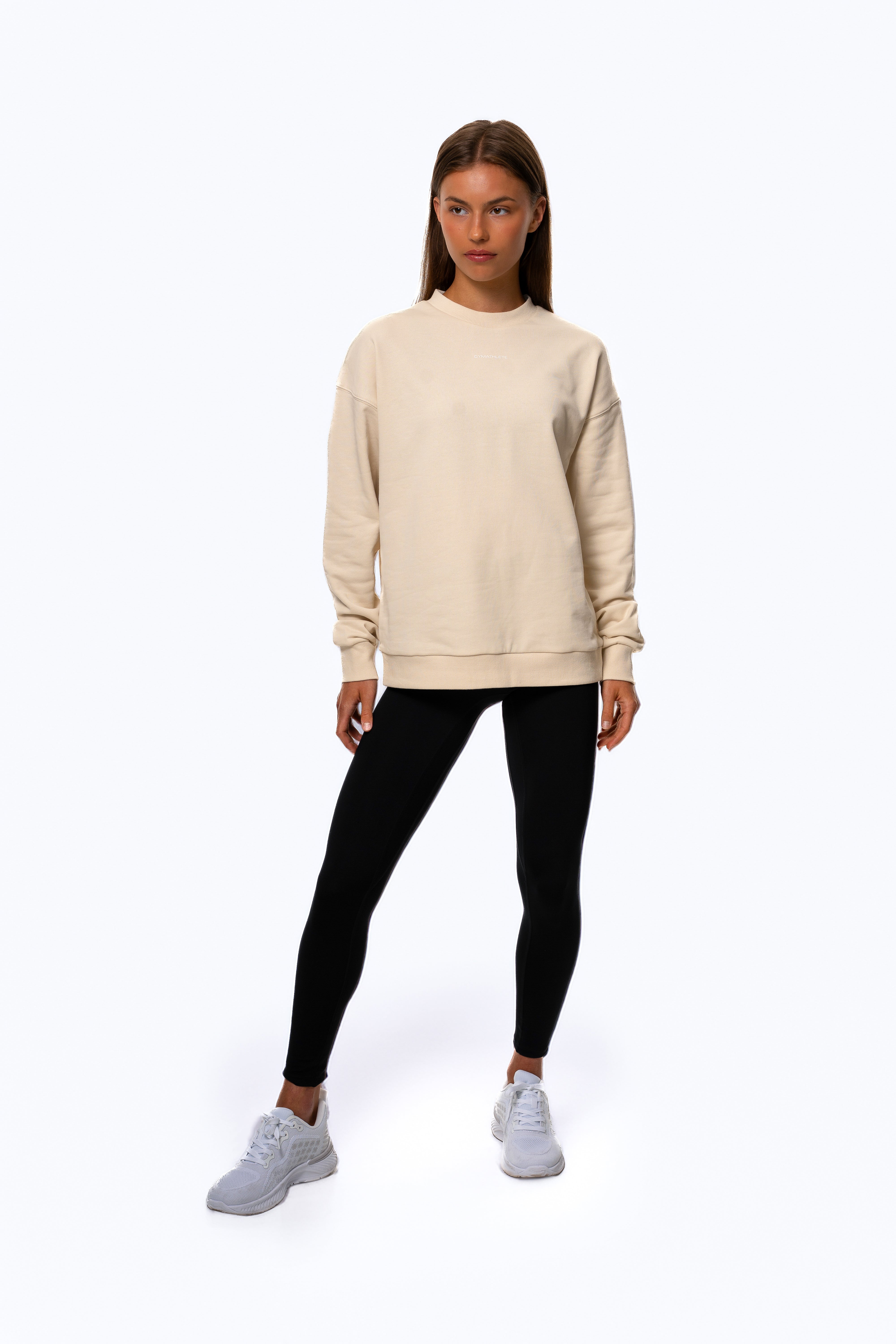 Woman wearing a beige sweatshirt and black leggings on a white background. Women - Gymathlete - Flow Sweatshirt - Beige.