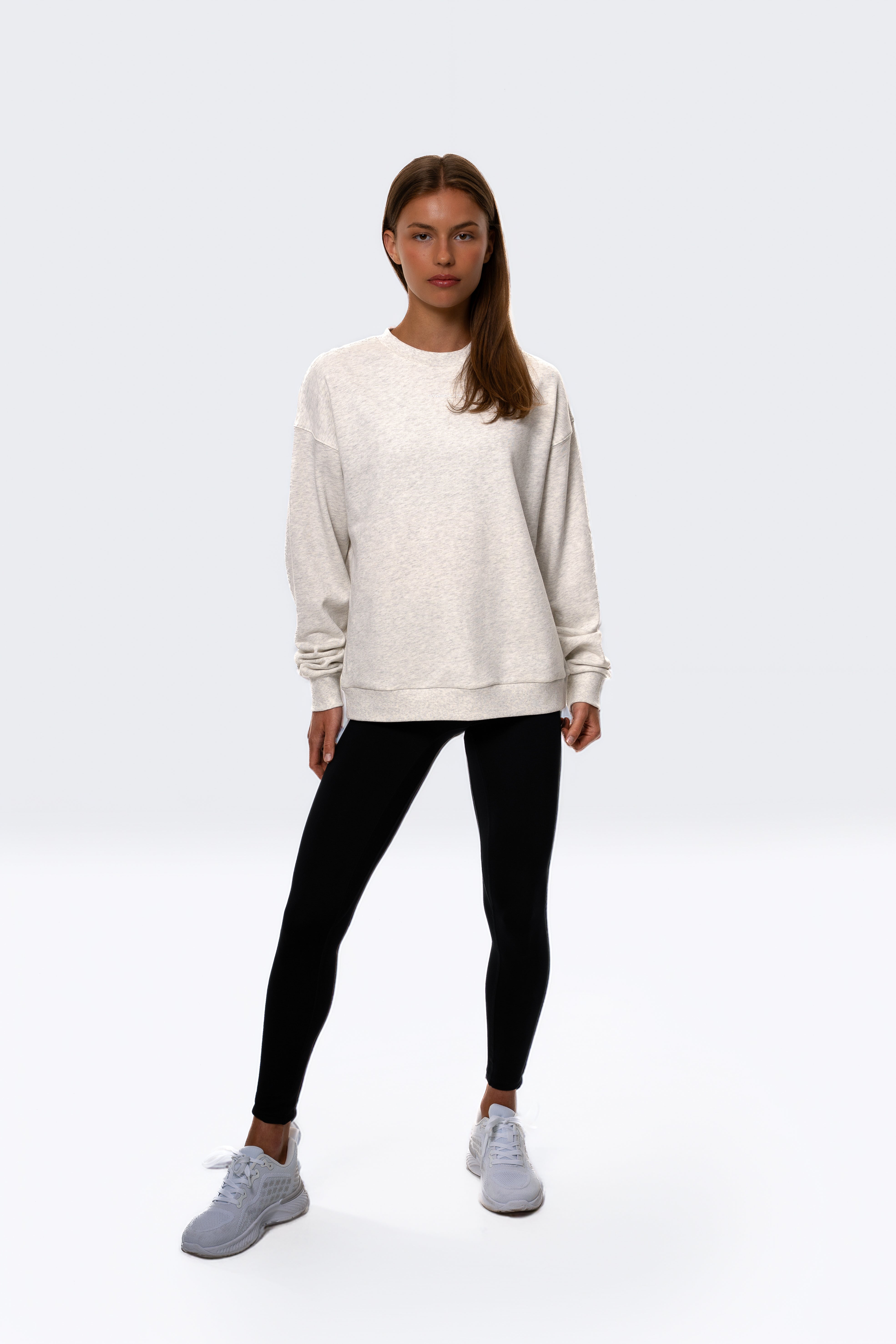 Woman wearing a beige sweatshirt, black leggings, and white sneakers on a white background. Women - Gymathlete - Flow Sweatshirt - White melange