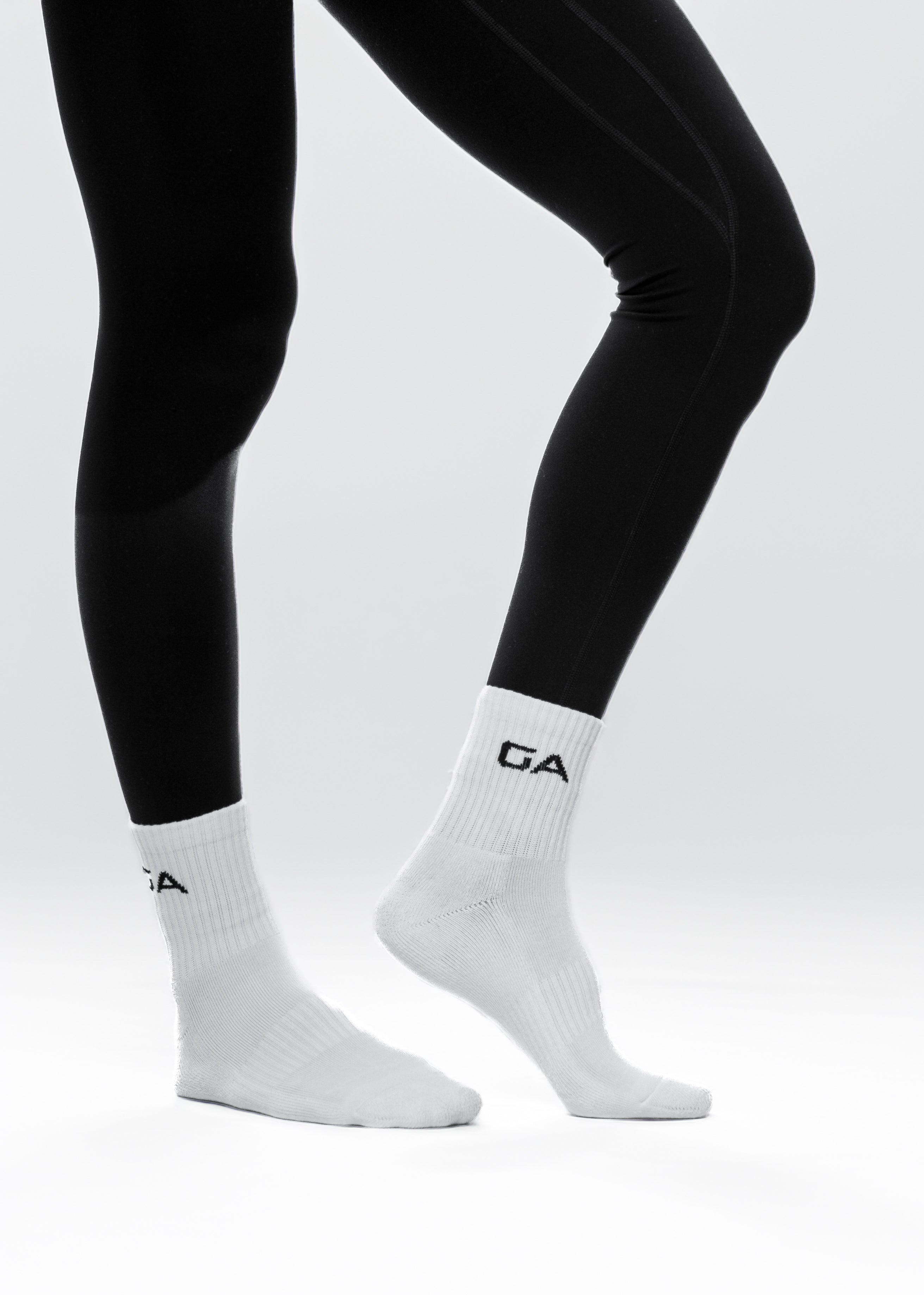 White socks with a logo worn with black leggings on a light gray background. GYMATHLETE - endurance socks