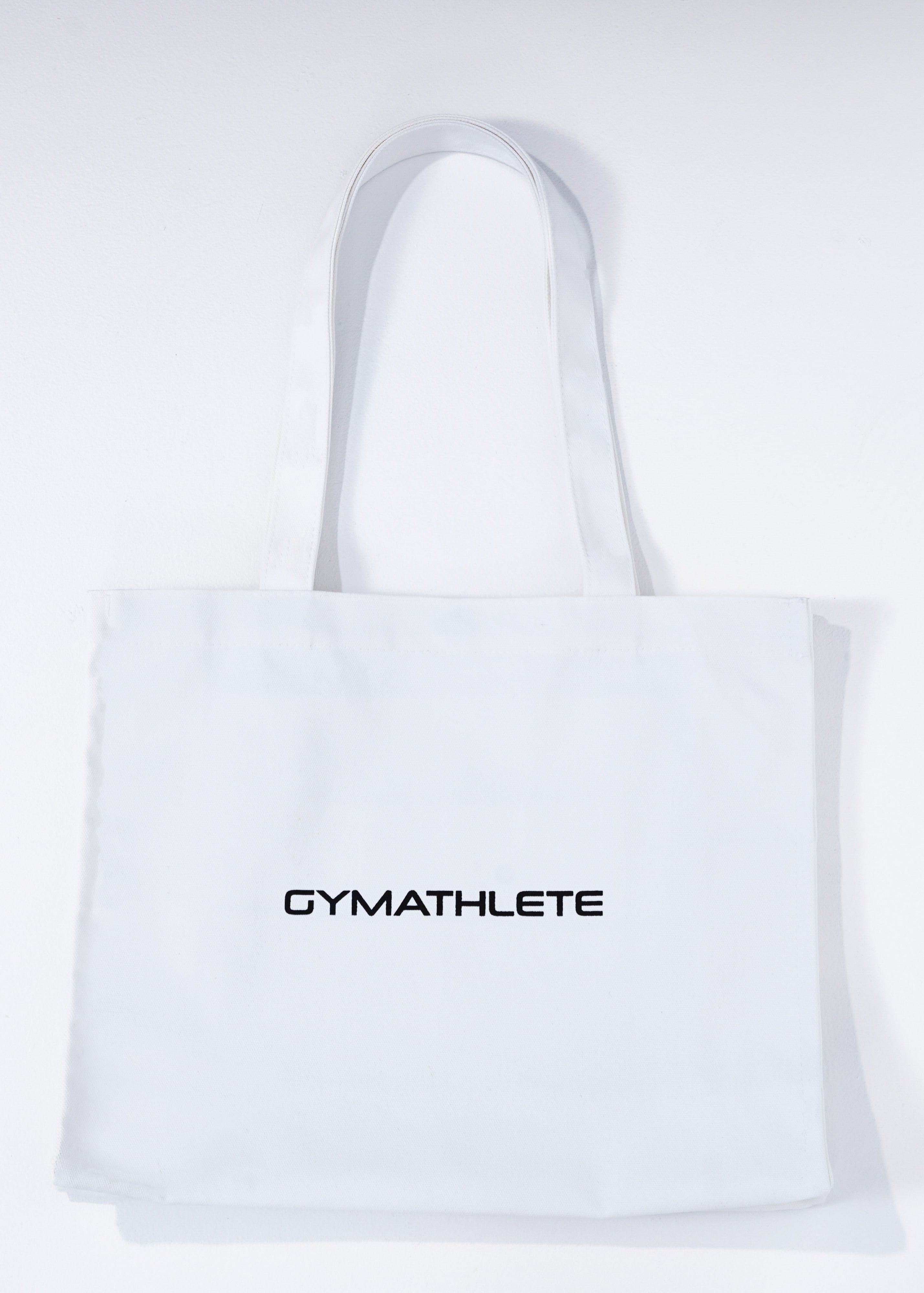 White tote bag with 'GYMATHLETE' branding on a light gray background. Balance Tote.