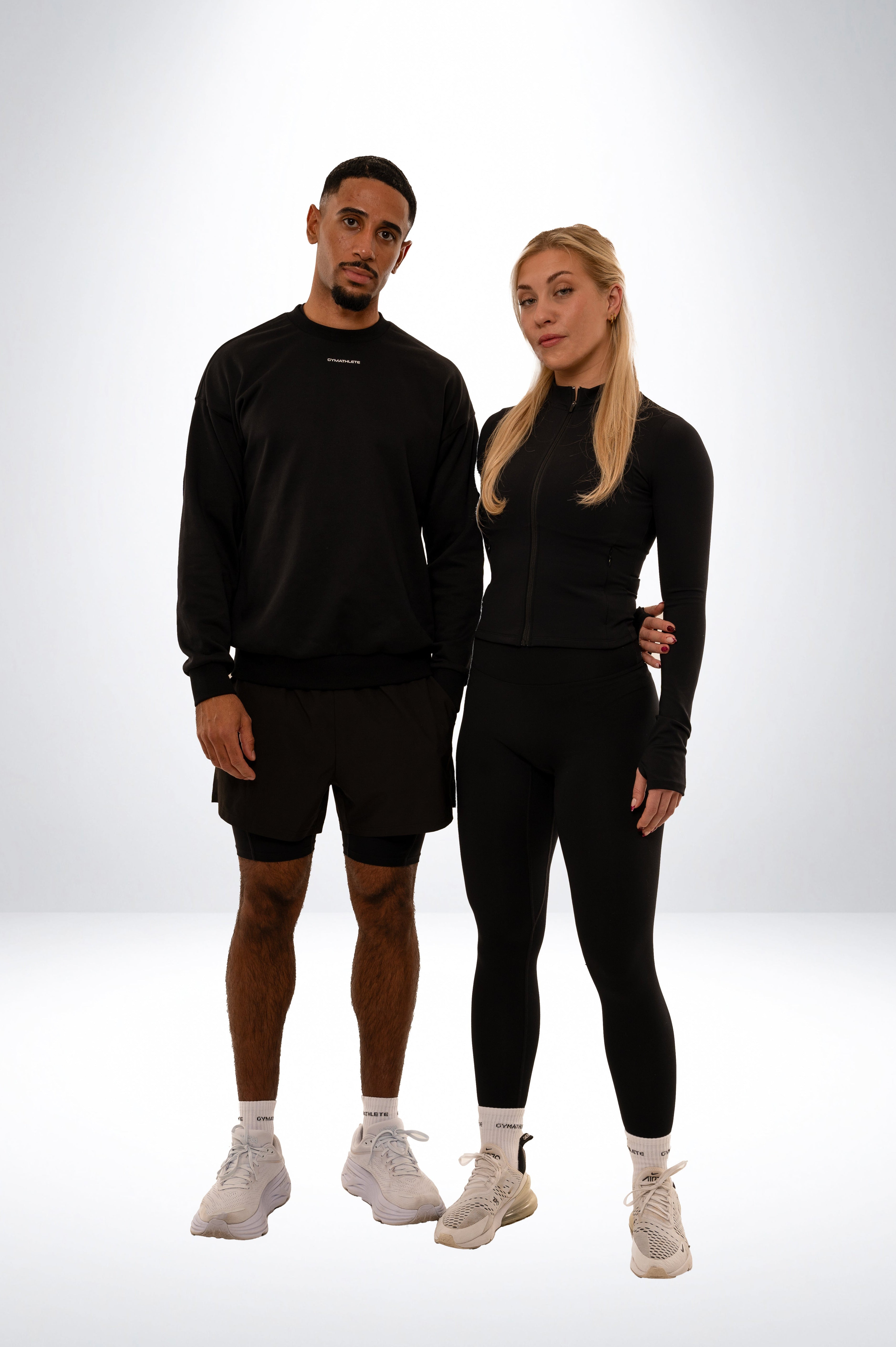 Two people wearing black athletic outfits on a white background. Gymathlete - Elevate Sweatshirt - 2IN1 SHORTS - PULSE LEGGINGS - ENDURANCE SOCKS - ZIP JACKET - Women - men