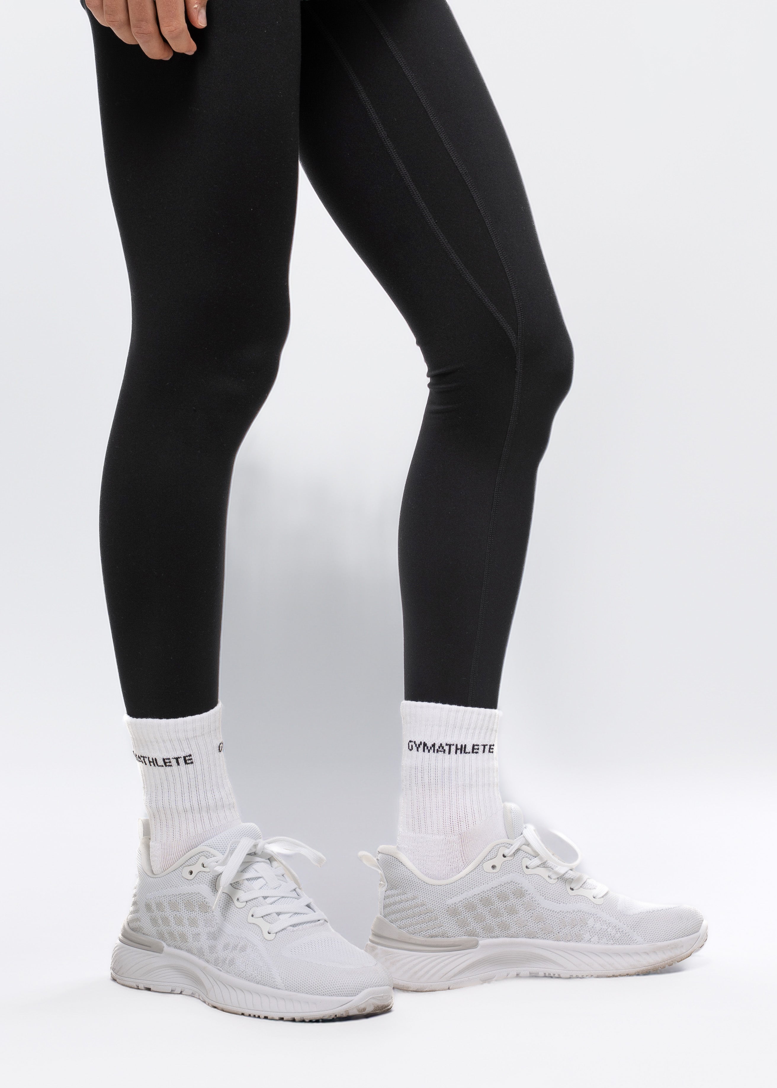 Person wearing black leggings and white sneakers on a light gray background. Gymathlete Endurance Socks