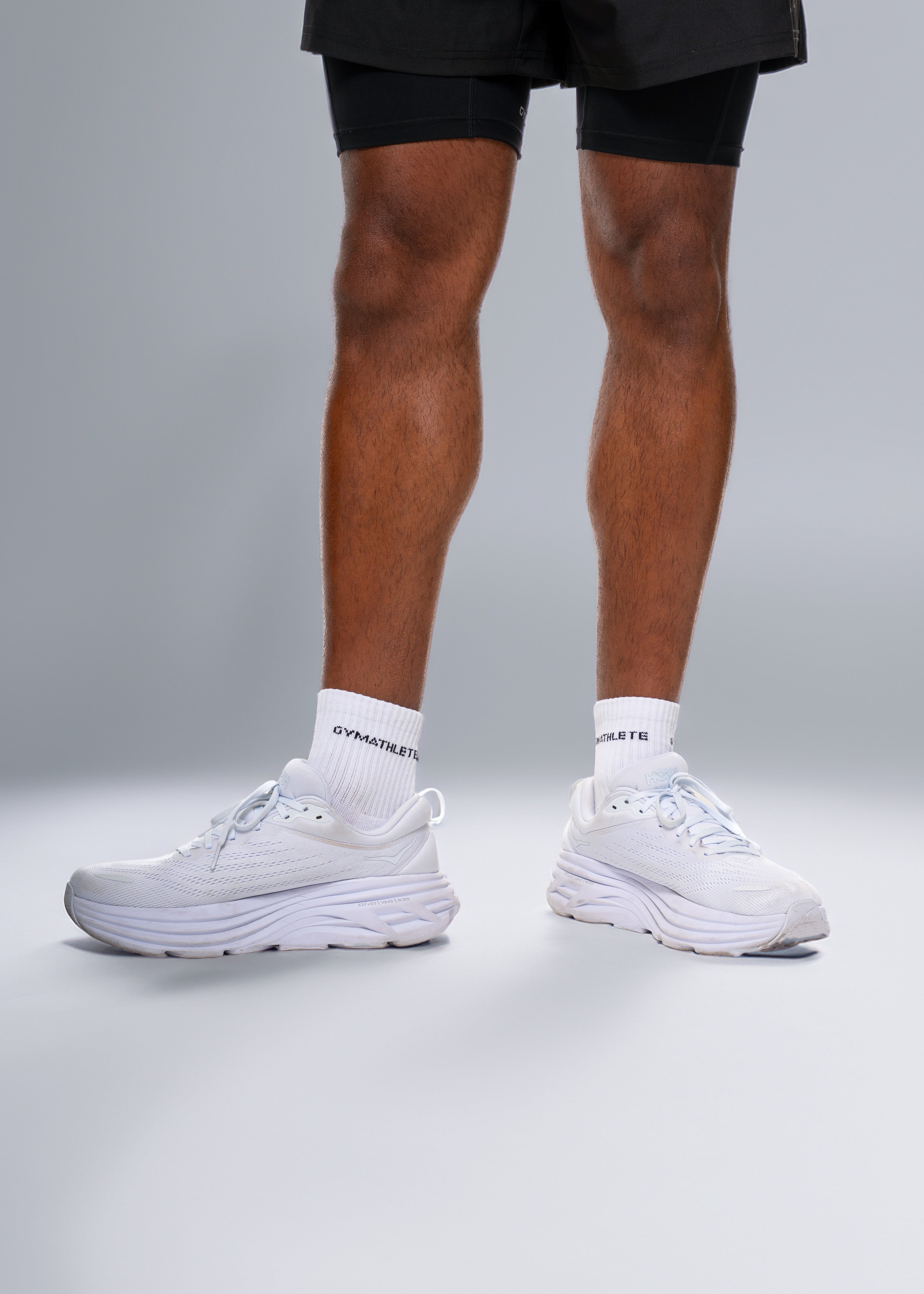 White sneakers worn with black shorts on a gray background - Gymathlete endurance socks 