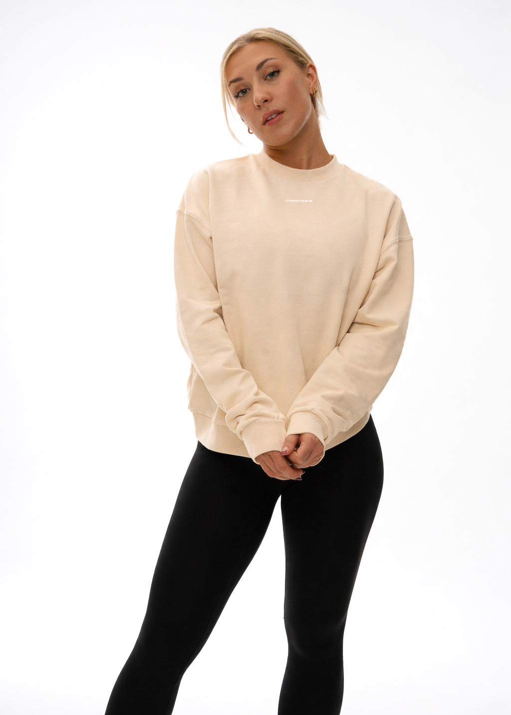 Woman wearing a beige sweatshirt and black pants on a white background. GYMATHLETE - WOMEN - SWEATSHIRT - ACTIVEWEAR.