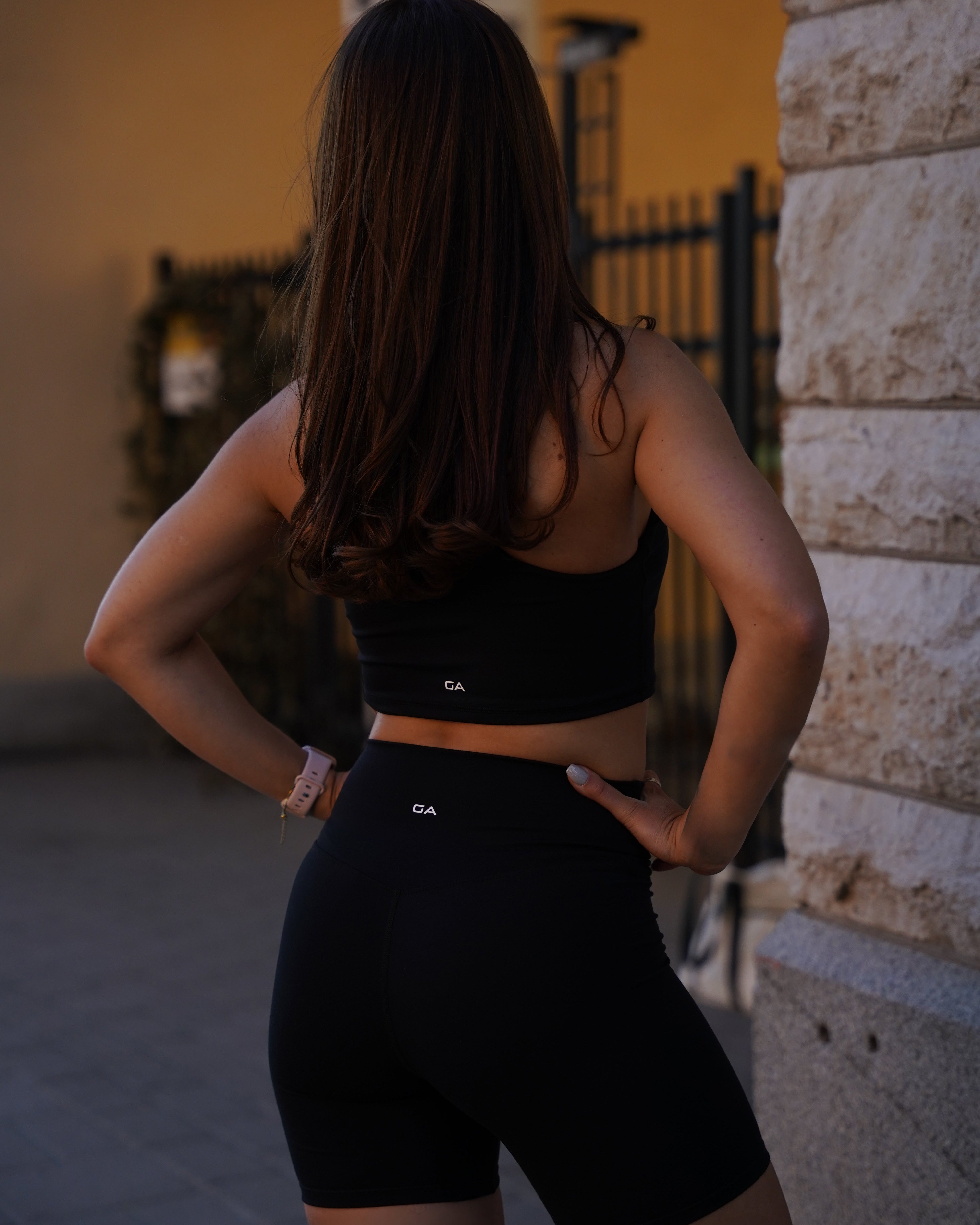 Back view of the black Gymathlete Pulse Crop Top and matching Pulse Shorts worn outdoors
